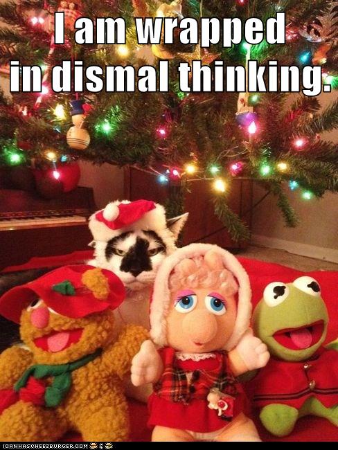 cat in Santa hat with Muppet toys under Christmas tree, looking unhappy
