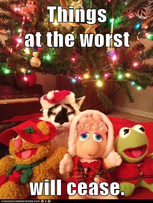 cat in santa hat with Muppet toys under Christmas tree, looking unhappy